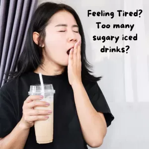 Woman yawning and holding a large iced coffee drink.